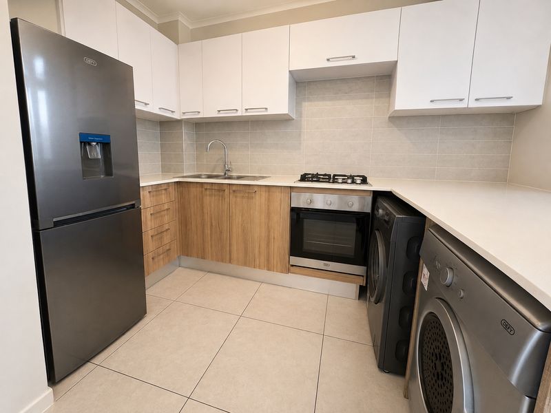 Modern kitchen featuring sleek white and wood-grain cabinetry, stone countertops, integrated gas hob, built-in oven, and neutral tiled flooring.