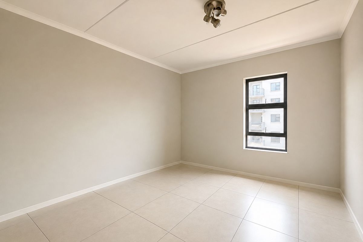 A bright, empty bedroom featuring neutral wall tones, large format floor tiles, and a modern ceiling-mounted spotlight fixture.