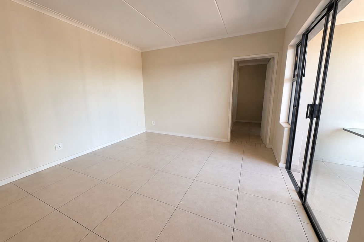 A bright, empty living room featuring neutral tiled flooring, clean walls, and a large sliding glass door providing access to the exterior.