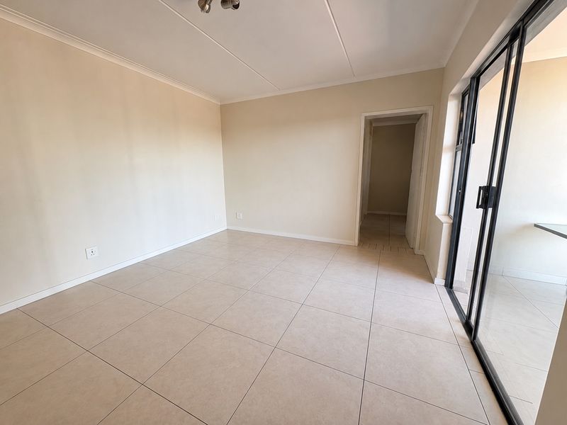 A bright, empty living room featuring neutral tiled flooring, clean walls, and a large sliding glass door providing access to the exterior.