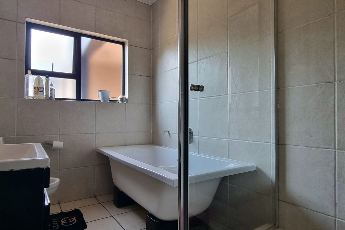 A functional bathroom featuring a freestanding bathtub, a separate glass-enclosed shower, and neutral wall tiling with a window for natural light.