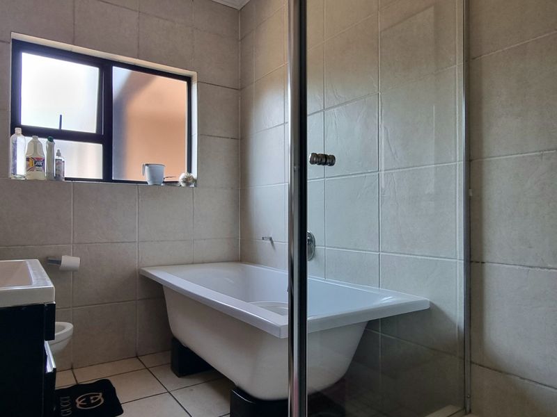 A functional bathroom featuring a freestanding bathtub, a separate glass-enclosed shower, and neutral wall tiling with a window for natural light.