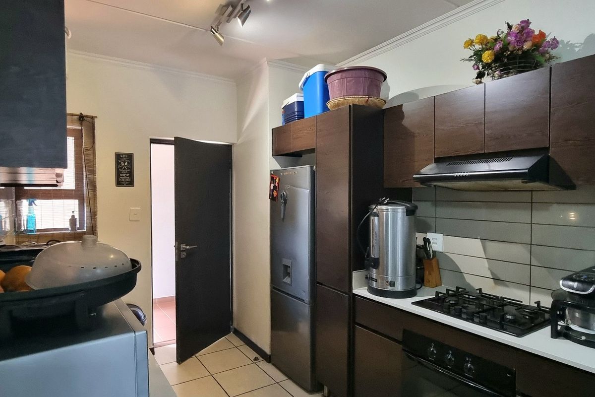 A functional kitchen featuring dark wood cabinetry, a gas hob, built-in oven, extractor fan, and tiled splashback with neutral floor tiles.