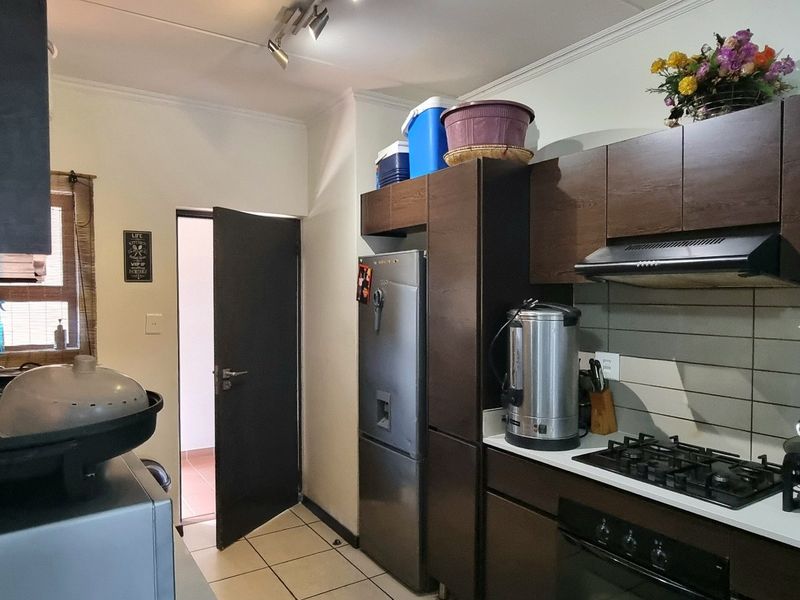 A functional kitchen featuring dark wood cabinetry, a gas hob, built-in oven, extractor fan, and tiled splashback with neutral floor tiles.