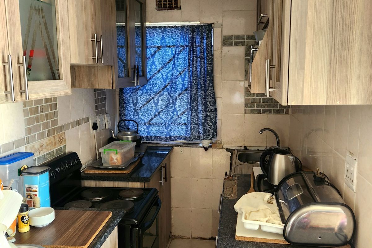 Compact galley kitchen featuring laminate cabinetry, tiled backsplash, and built-in cooking appliances, offering a functional layout in need of cosmetic updates.