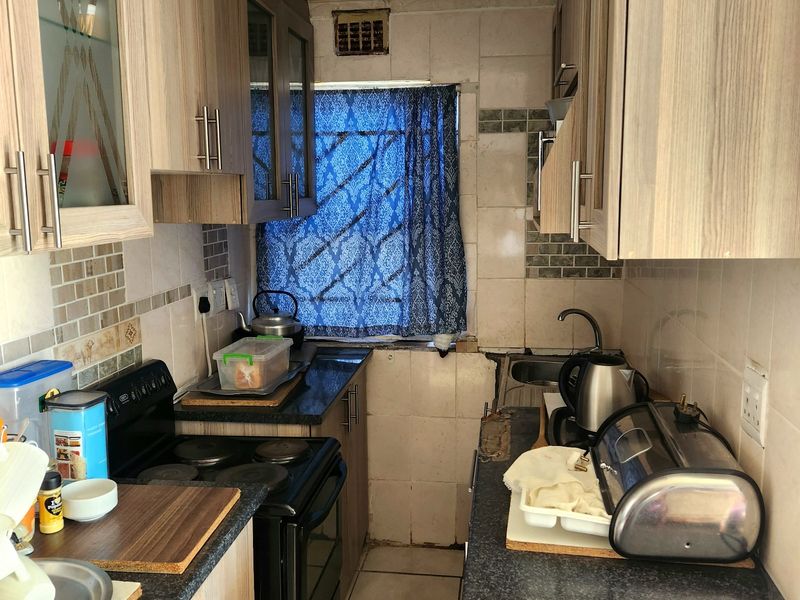 Compact galley kitchen featuring laminate cabinetry, tiled backsplash, and built-in cooking appliances, offering a functional layout in need of cosmetic updates.
