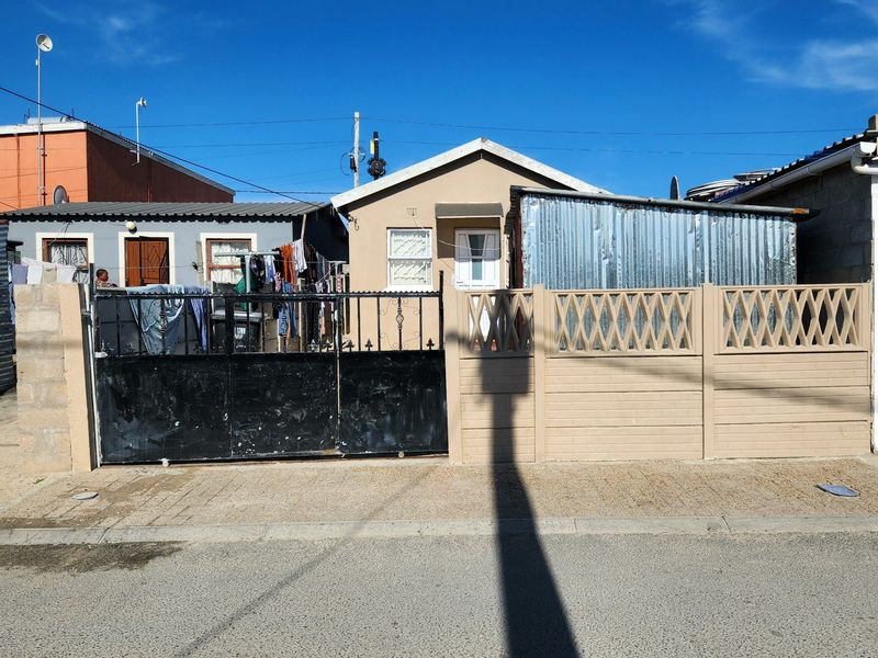 Front elevation of a residential property featuring a gated entrance, paved driveway, and a precast concrete boundary wall with corrugated metal side structure.