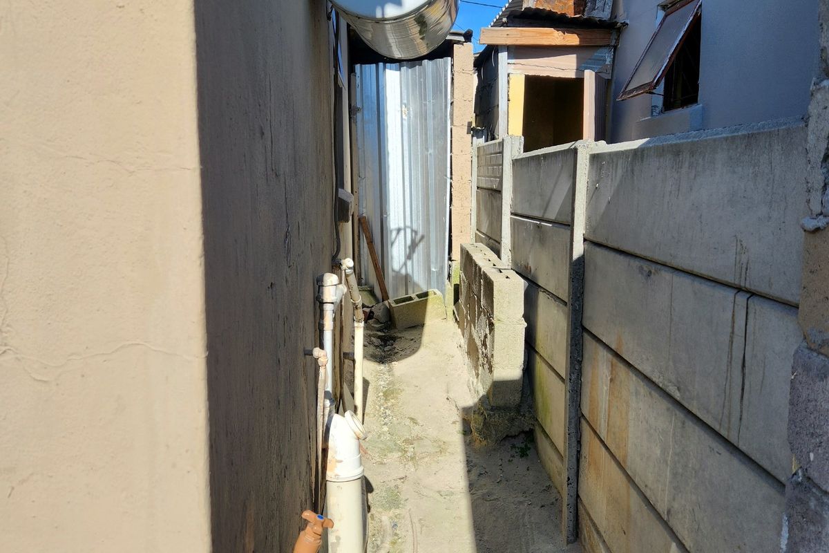 A narrow side passage featuring an external geyser, exposed plumbing, and a precast concrete boundary wall.