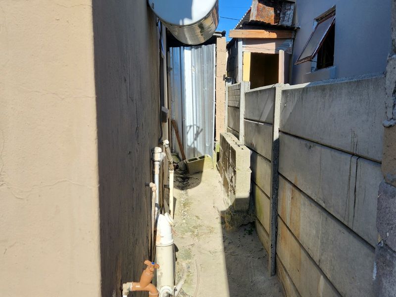 A narrow side passage featuring an external geyser, exposed plumbing, and a precast concrete boundary wall.