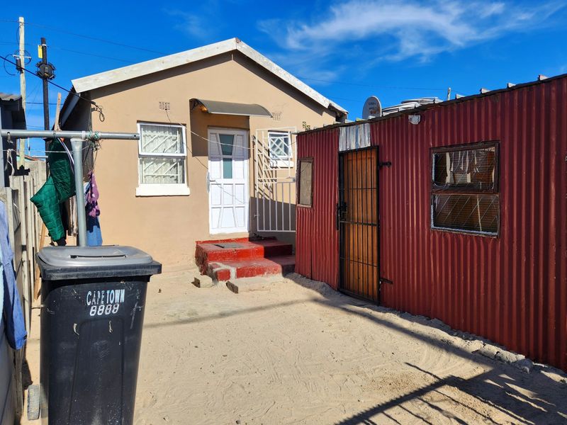 Rear exterior view of the property featuring a main dwelling with security gates and an adjacent corrugated iron structure.