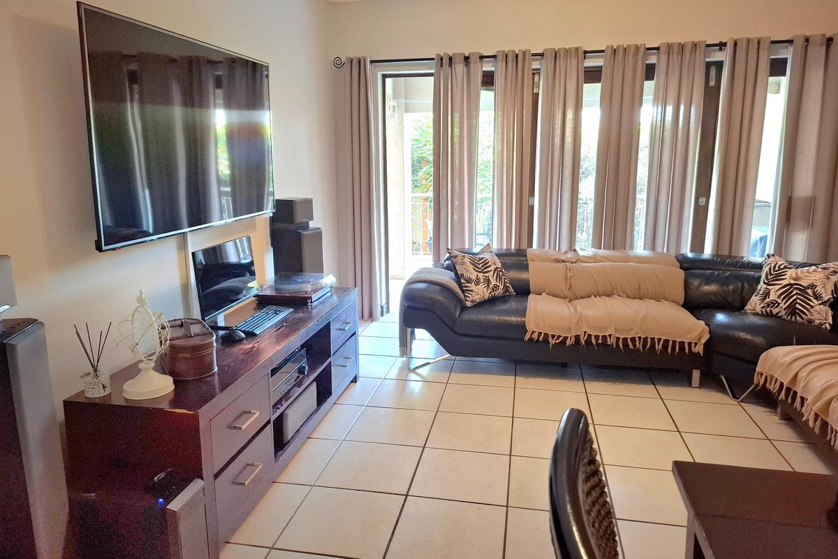 A well-maintained living room featuring ceramic floor tiles, coving, and large sliding glass doors that provide access to an outdoor area.