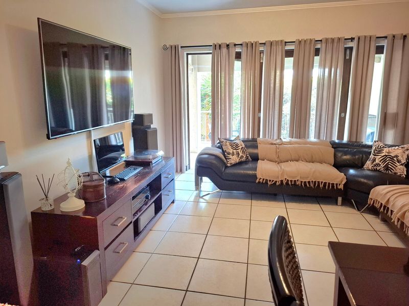 A well-maintained living room featuring ceramic floor tiles, coving, and large sliding glass doors that provide access to an outdoor area.