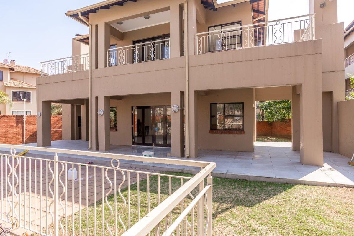 Rear view of the apartment building featuring a covered ground-floor patio, an upper-level balcony with metal railings, and access to a private garden area.