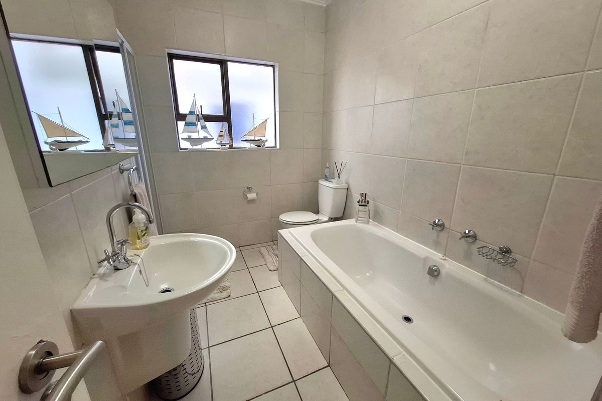 A clean, functional bathroom featuring a pedestal basin, built-in bathtub, and neutral wall and floor tiling.