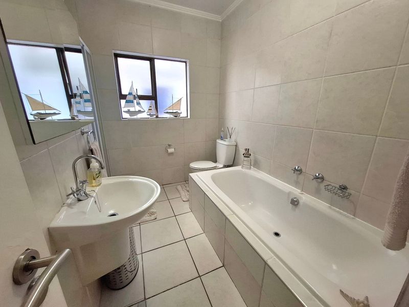 A clean, functional bathroom featuring a pedestal basin, built-in bathtub, and neutral wall and floor tiling.