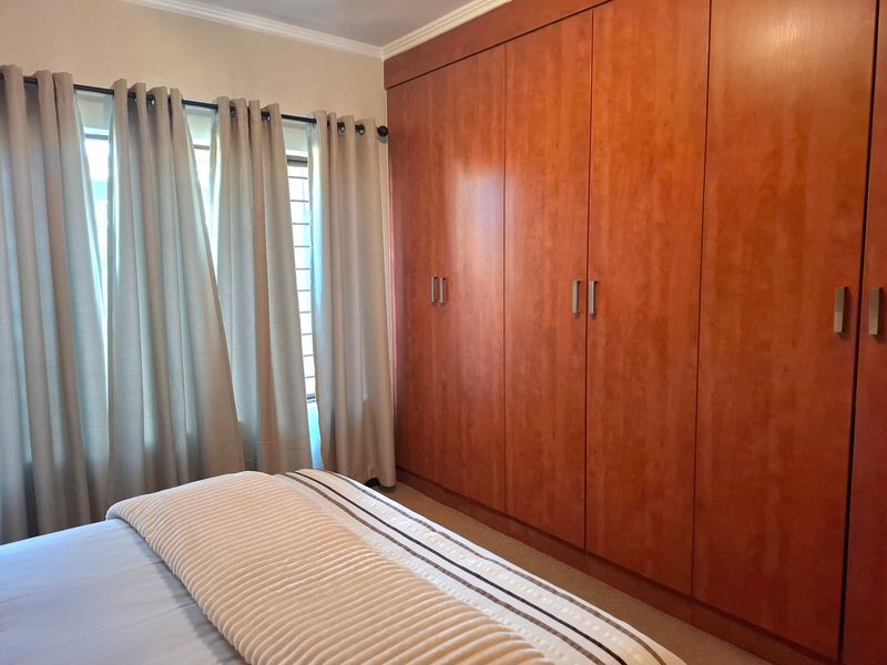 A well-maintained bedroom featuring extensive floor-to-ceiling built-in wooden cupboards and neutral finishes, providing ample storage space.