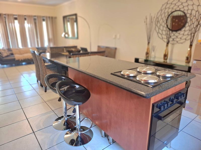 Open plan living area featuring a kitchen island with built-in oven and electric hob, seamlessly connecting to the dining and lounge space.