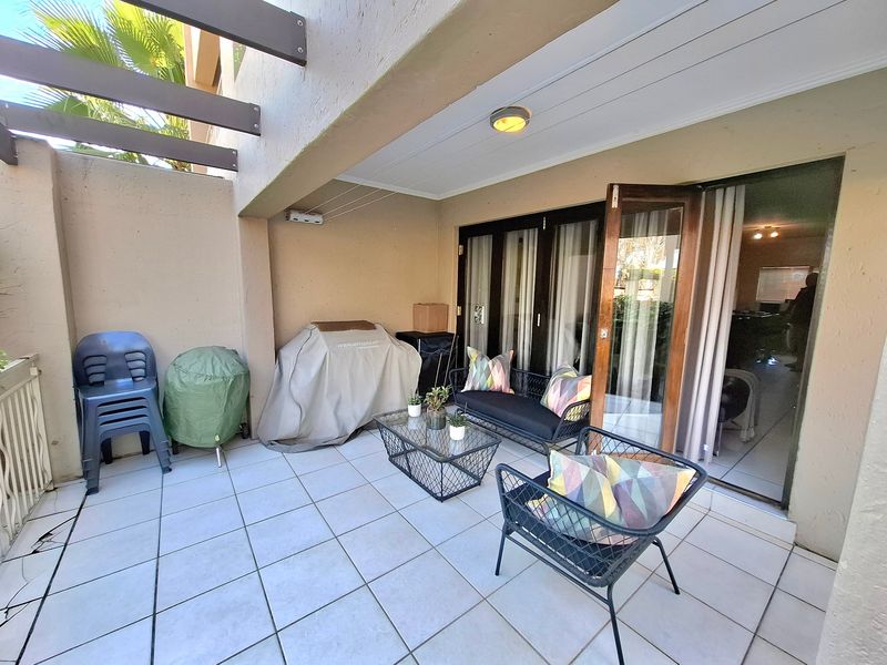 Covered patio area featuring tiled flooring, a timber pergola structure, and direct access to the interior through double glass doors.