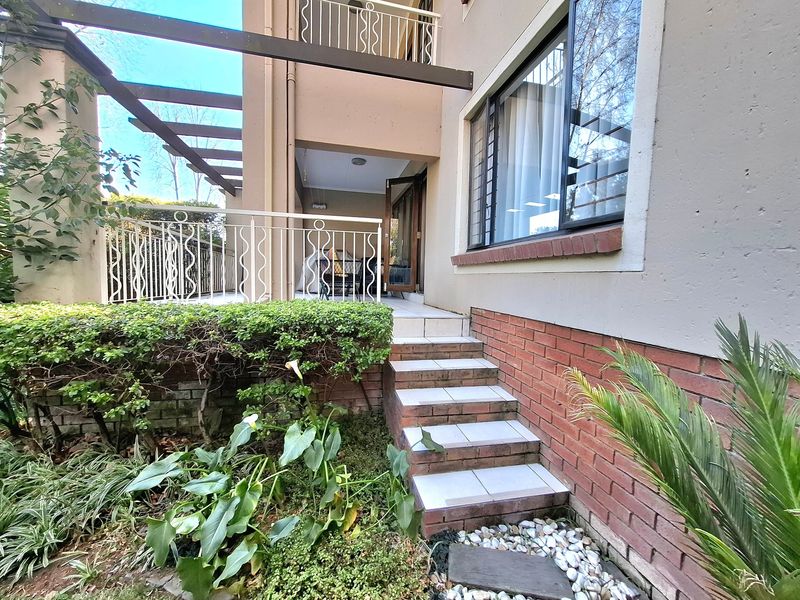 Rear exterior view of the apartment featuring a tiled patio, timber pergola, metal balustrades, and direct access via sliding glass doors.