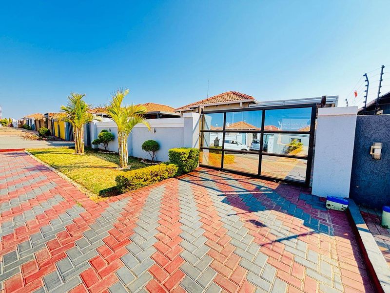 Front view of the property featuring a paved driveway, secure boundary wall with electric fencing, and a modern sliding gate.
