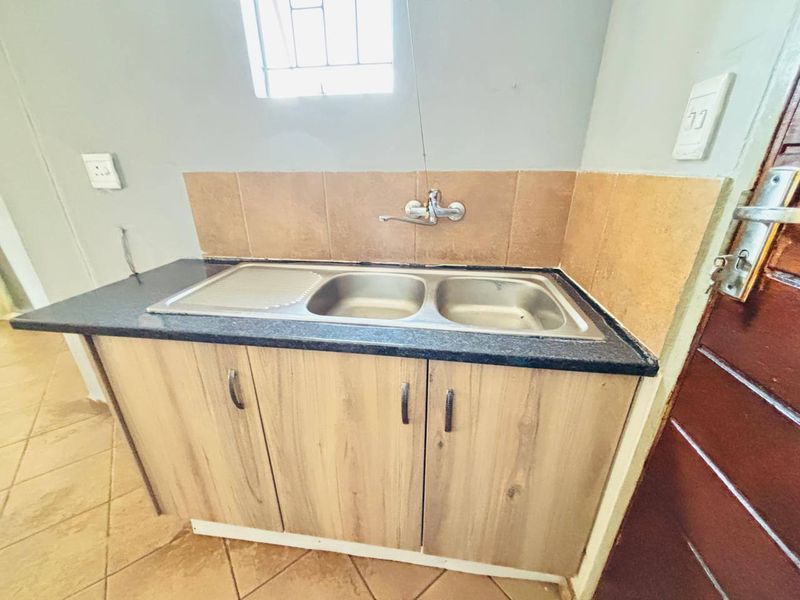 A functional scullery area featuring a double bowl stainless steel sink, laminate cabinetry, and tiled splashback, providing a practical utility space.