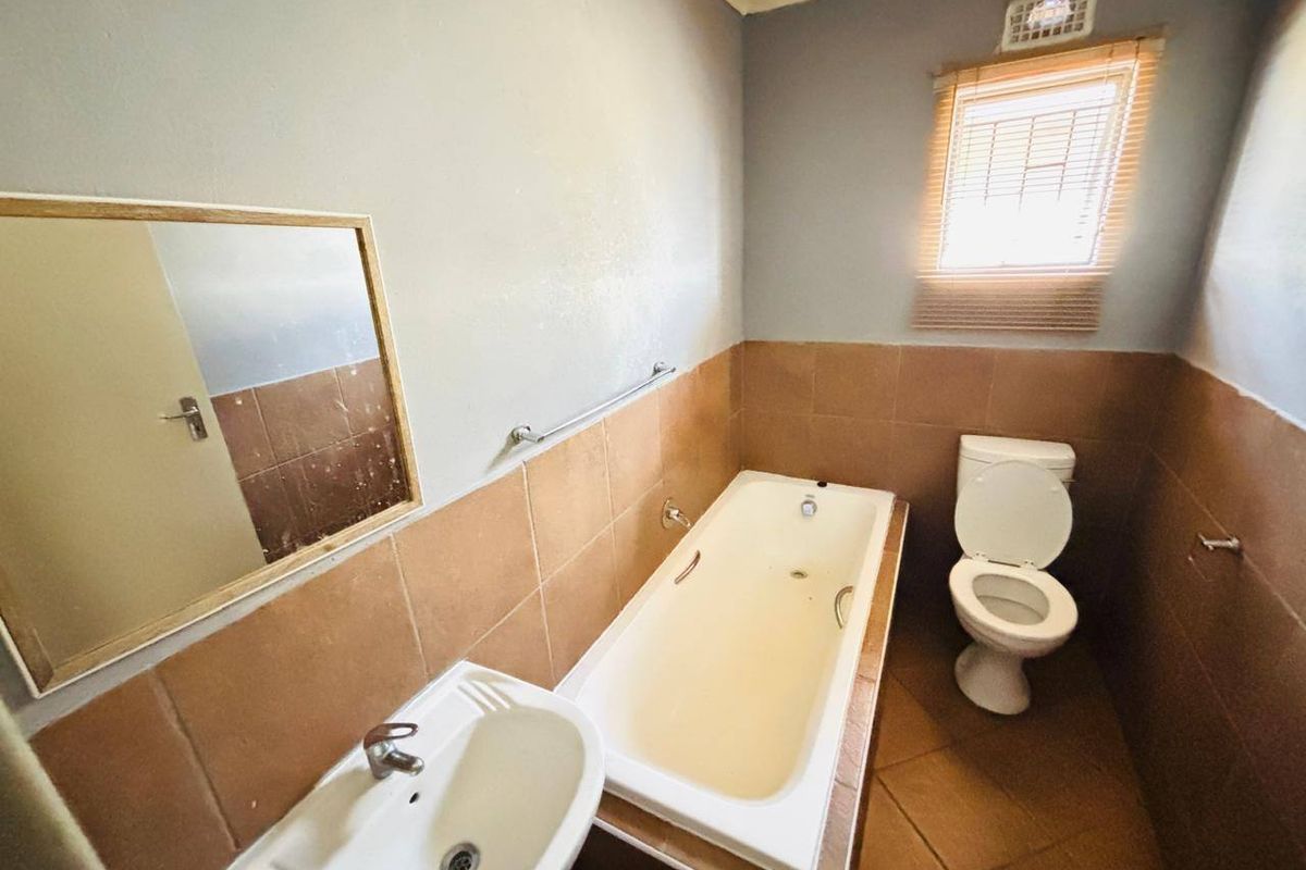 A functional bathroom featuring a bathtub, pedestal basin, and toilet with neutral wall and floor tiling, ready for cosmetic updates.