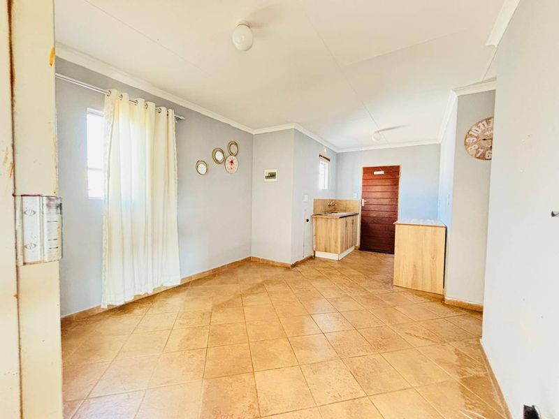 An open-plan living area featuring tiled flooring and a compact kitchenette with built-in cabinetry and a sink.