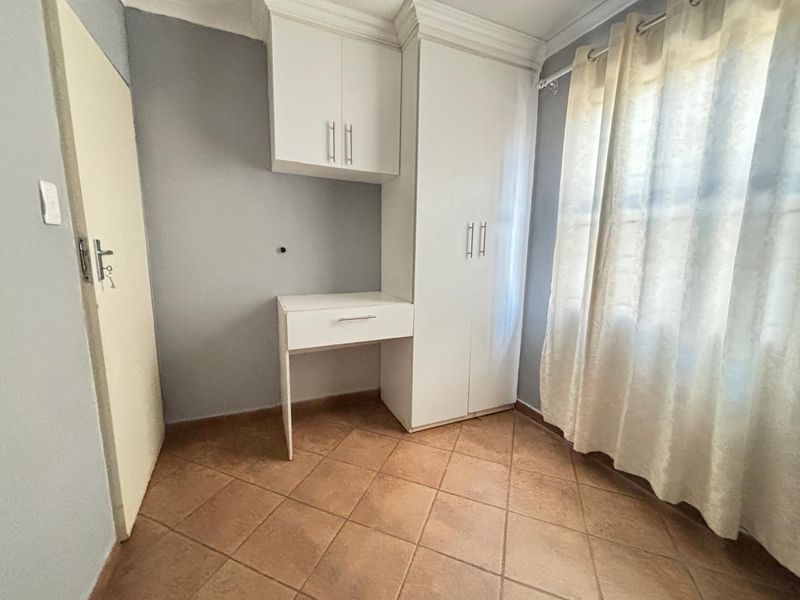 A bedroom featuring built-in cabinetry, a desk, tiled flooring, and crown molding, presenting a clean and functional space.