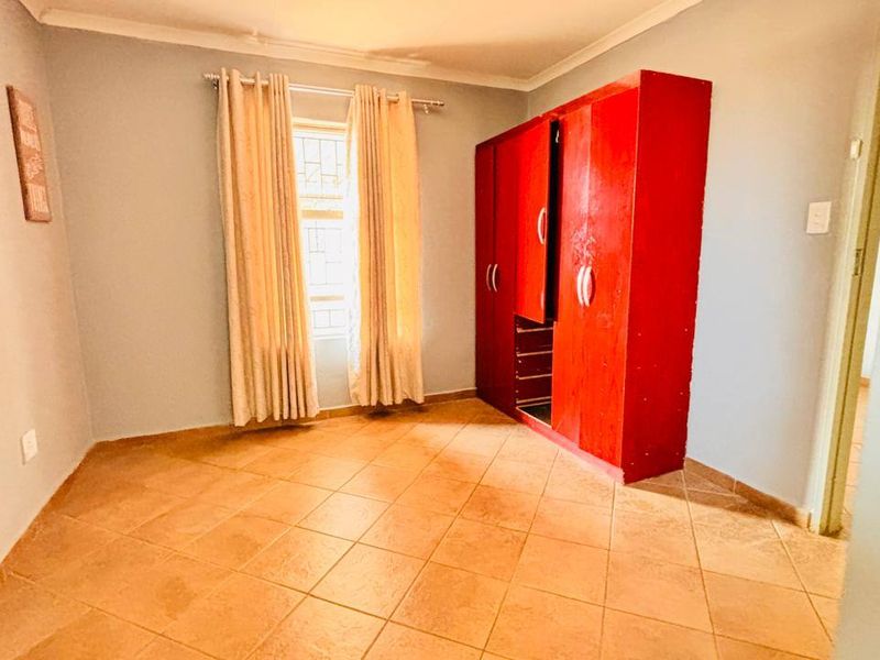 A bedroom featuring tiled flooring, a built-in wardrobe, and a window with security bars, offering a clean and functional space.