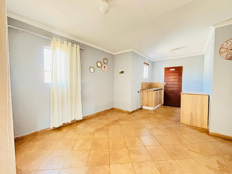 An open-plan living area featuring tiled flooring, a compact kitchenette with built-in cabinetry and sink, and direct access to an exterior door.