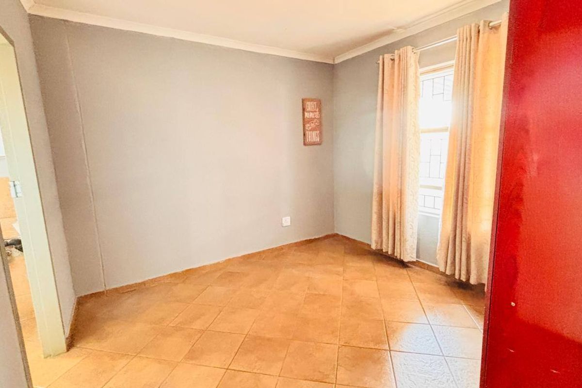 A bright, empty bedroom featuring neutral wall tones, tiled flooring, and security bars on the window, offering a clean canvas for personalization.