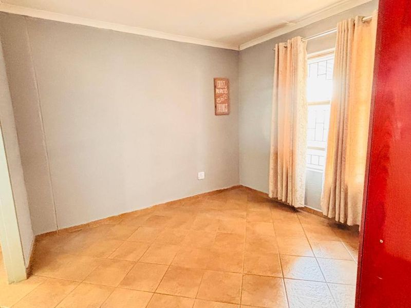 A bright, empty bedroom featuring neutral wall tones, tiled flooring, and security bars on the window, offering a clean canvas for personalization.