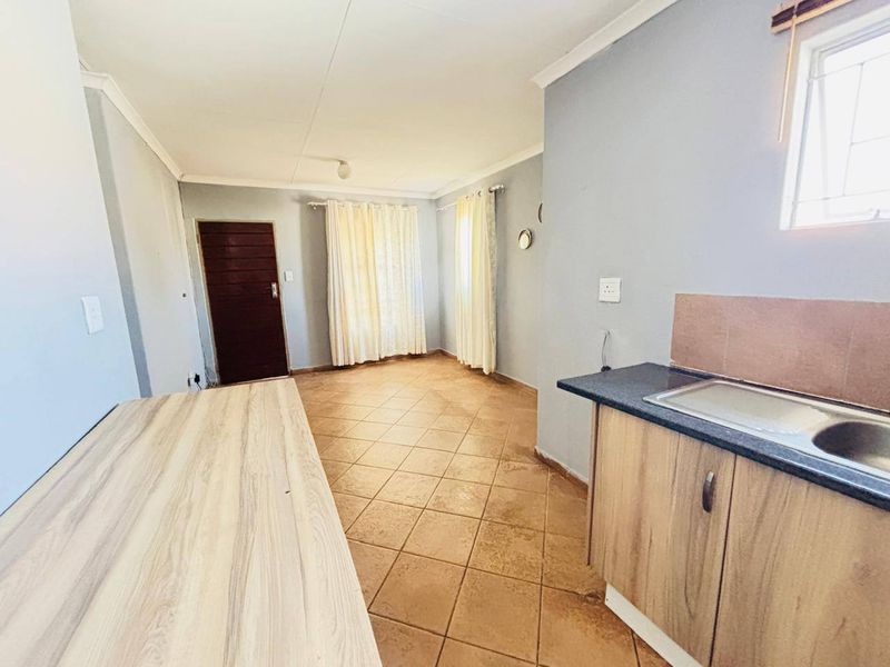 An open-plan living and kitchen area featuring tiled flooring, built-in cabinetry with a laminate countertop, and a stainless steel sink.