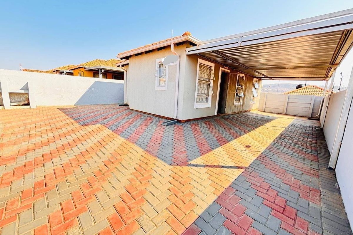 A paved rear exterior area featuring a covered carport, secure boundary walls, and tiled roof structure.