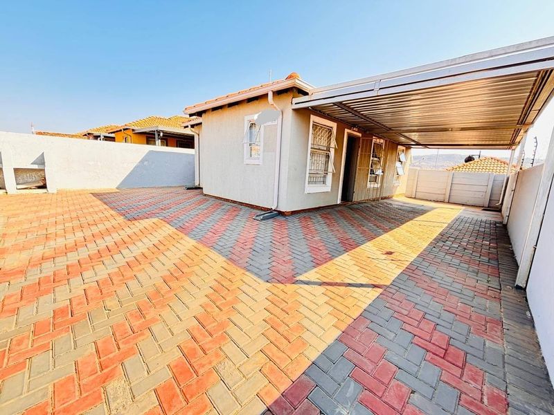 A paved rear exterior area featuring a covered carport, secure boundary walls, and tiled roof structure.