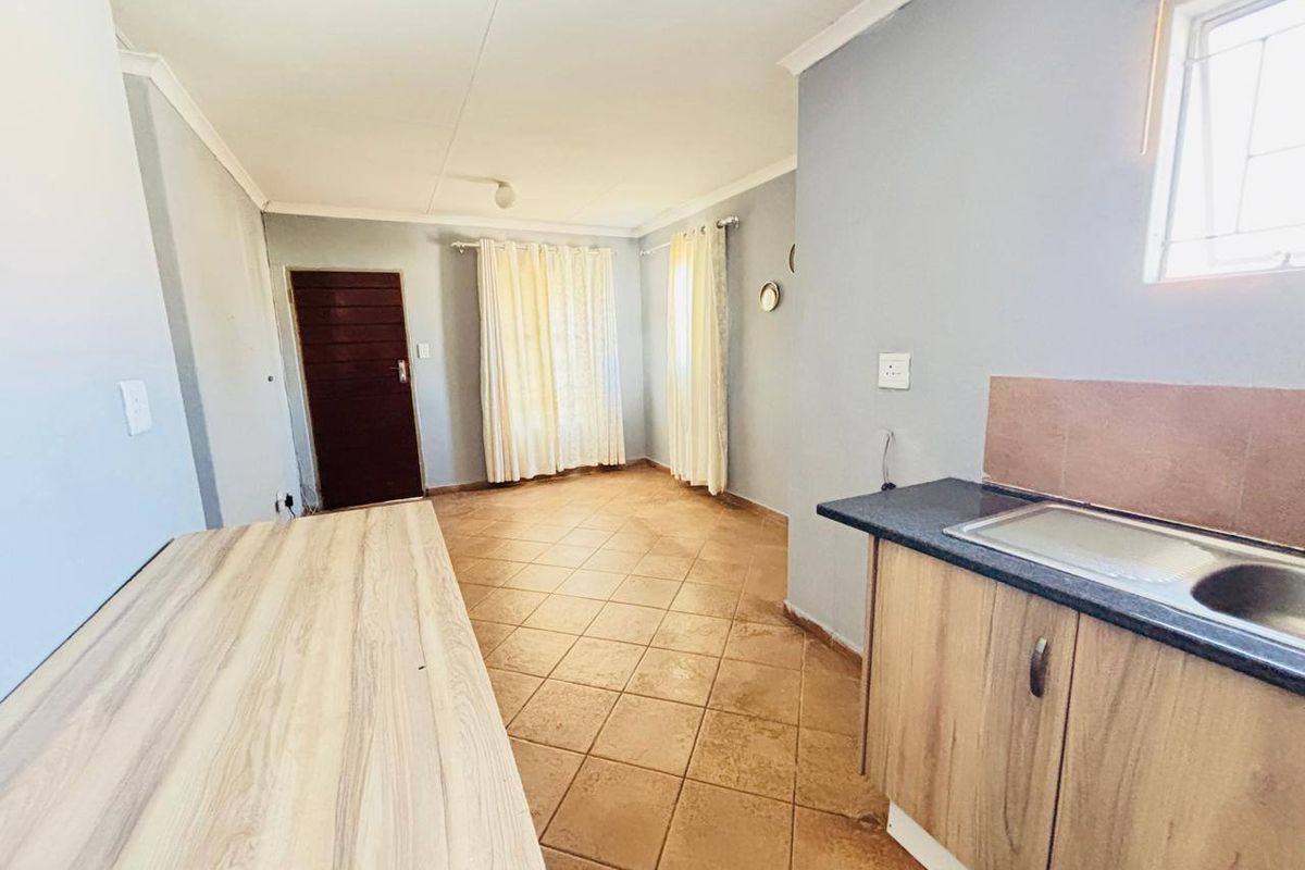 An open-plan living and kitchen area featuring tiled flooring, built-in cabinetry with a laminate countertop, and a stainless steel sink.