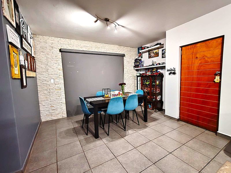 A dining area featuring a textured stone accent wall, neutral tiled flooring, and a modern wooden door, providing a functional and well-maintained space.