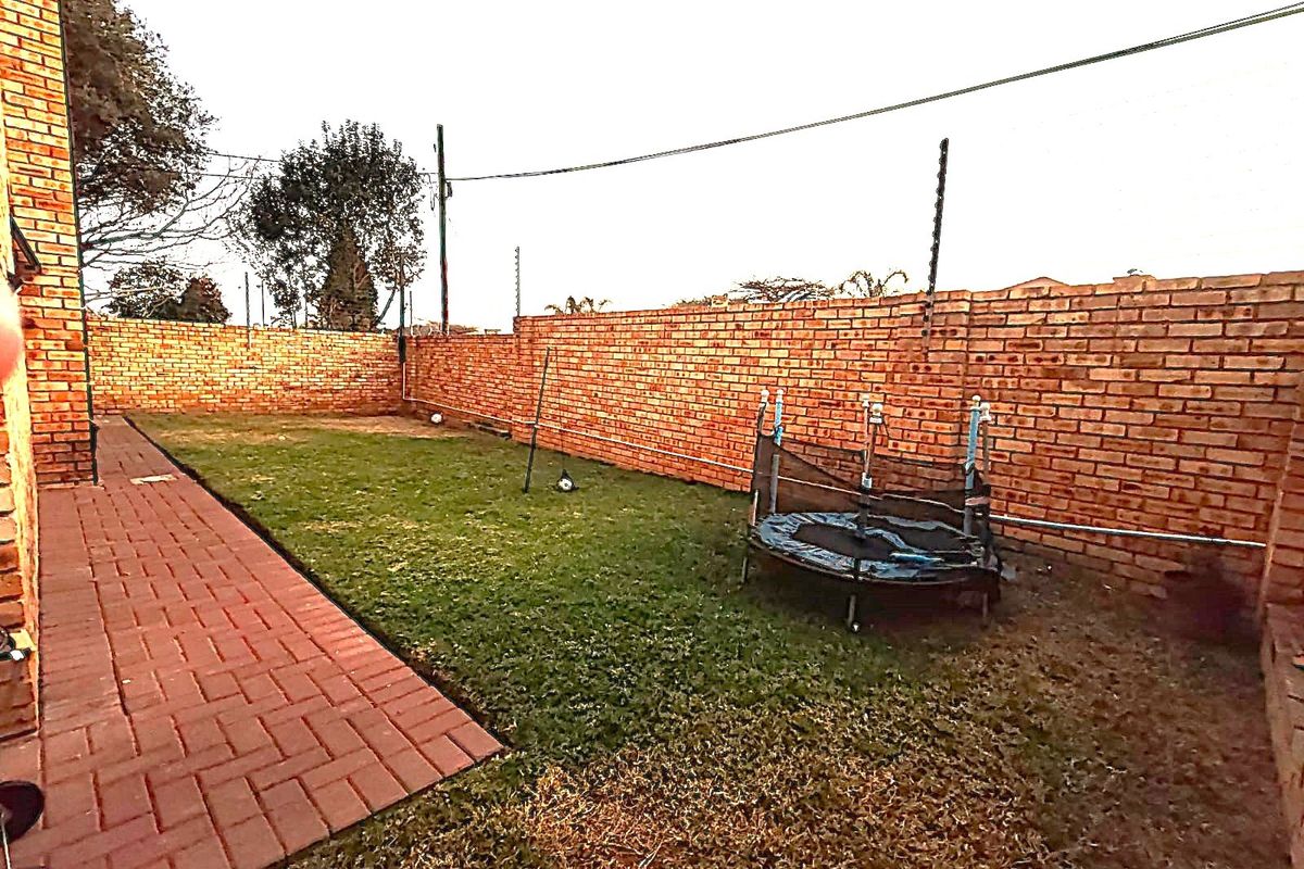 A private rear garden featuring a brick boundary wall with electric fencing and a paved walkway leading along the side of the property.