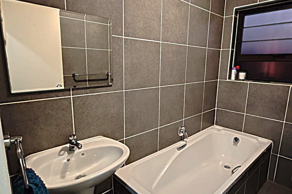 A compact bathroom featuring dark tiled walls, a white pedestal basin, and a built-in bathtub with matching tiled surround.