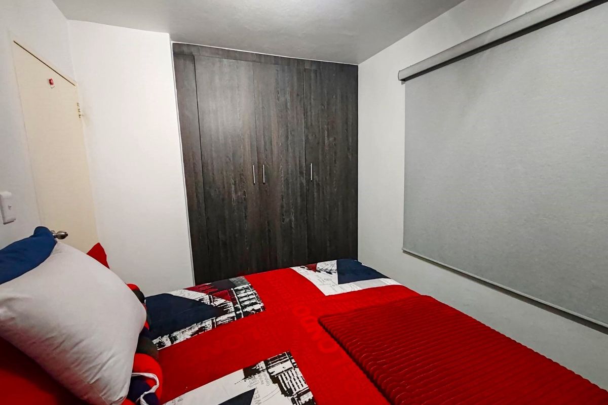 A functional bedroom featuring a dark wood-finish built-in wardrobe and a neutral roller blind, providing essential storage and privacy.