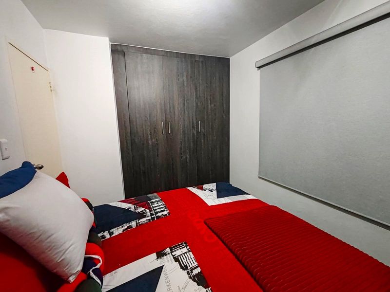 A functional bedroom featuring a dark wood-finish built-in wardrobe and a neutral roller blind, providing essential storage and privacy.