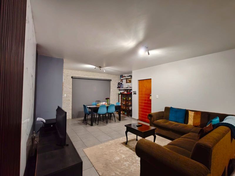Spacious open-plan living and dining area featuring tiled flooring, a textured stone accent wall, and neutral finishes throughout.