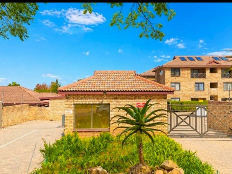 Front entrance view of the apartment complex featuring face brick architecture, a security guard house, paved driveway, and secure gated access.