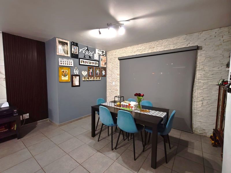 A well-maintained dining area featuring a textured stone veneer accent wall, neutral floor tiles, and a modern roller blind.