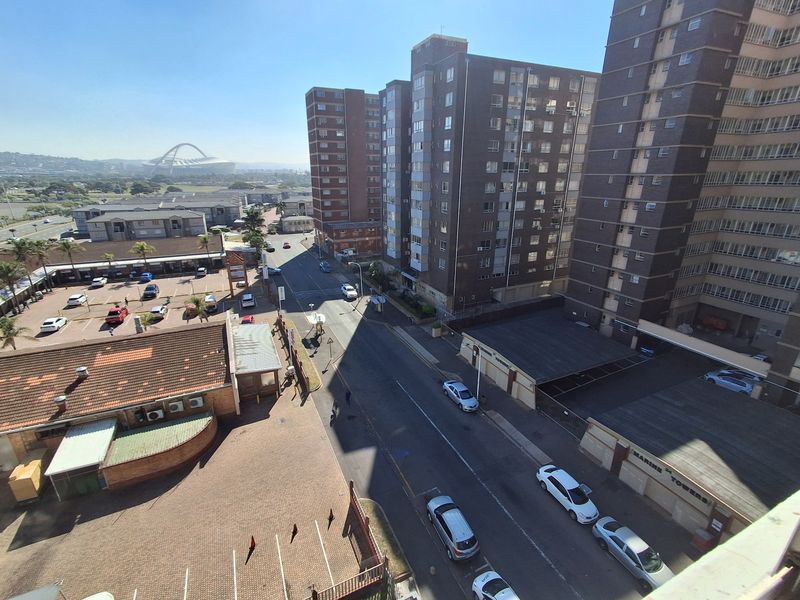 An elevated urban view overlooking a street, parking area, and surrounding high-rise apartment buildings.