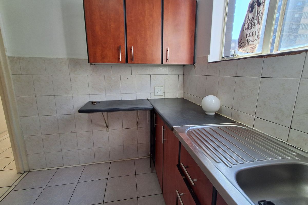 A functional kitchen area featuring wood-look cabinetry, dark laminate countertops, a stainless steel sink, and neutral ceramic wall and floor tiling.