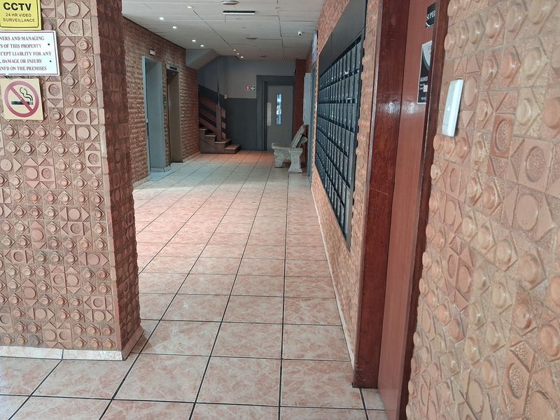 A communal apartment building hallway featuring textured brick walls, ceramic tiled flooring, a bank of mailboxes, and access to elevators and stairs.