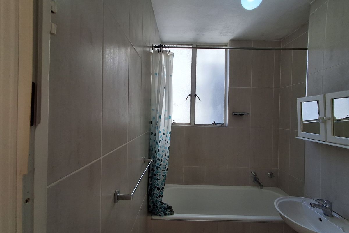 A functional bathroom featuring a bathtub, wall-mounted basin, and tiled walls, offering a neutral base ready for modern updates.