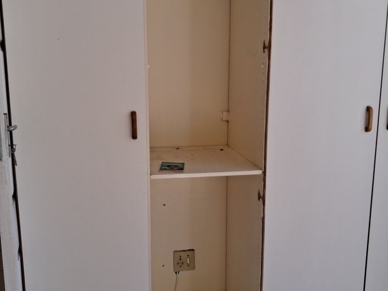 A bedroom featuring a built-in wardrobe with a missing central door panel, revealing internal shelving and an electrical outlet.