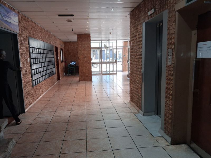 Spacious apartment building entrance lobby featuring tiled flooring, integrated mailboxes, and elevator access with a functional, dated design.